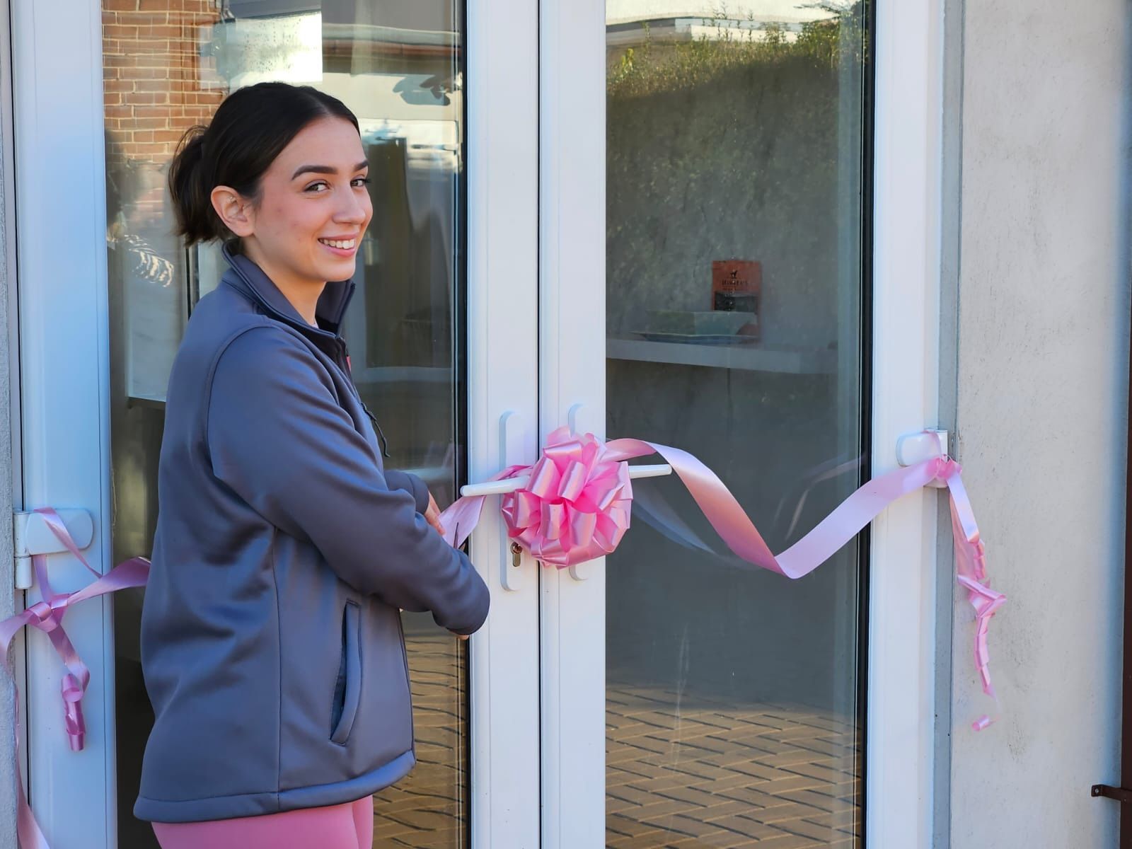 A canine hydrotherapist cutting a pink ribbon on a door, opening a centre.